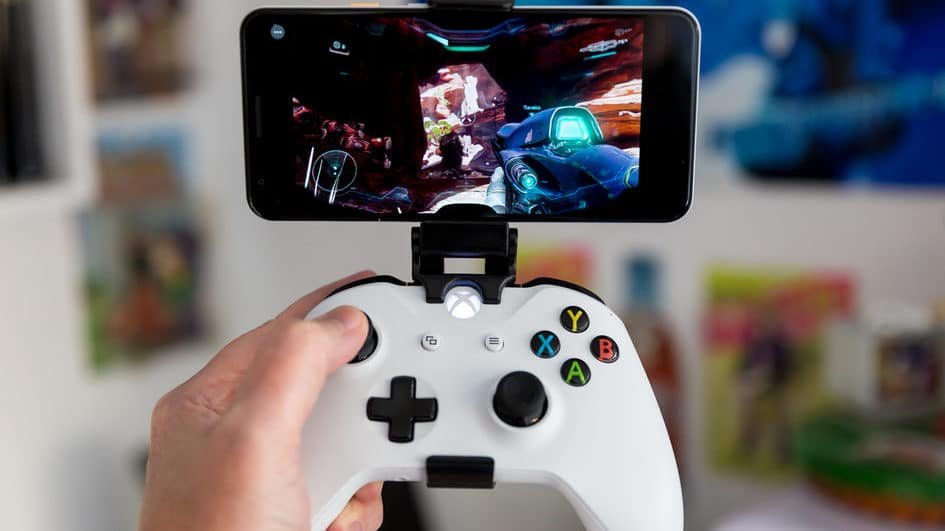 Person holding a smartphone with an Xbox controller nearby, showing a streamed game