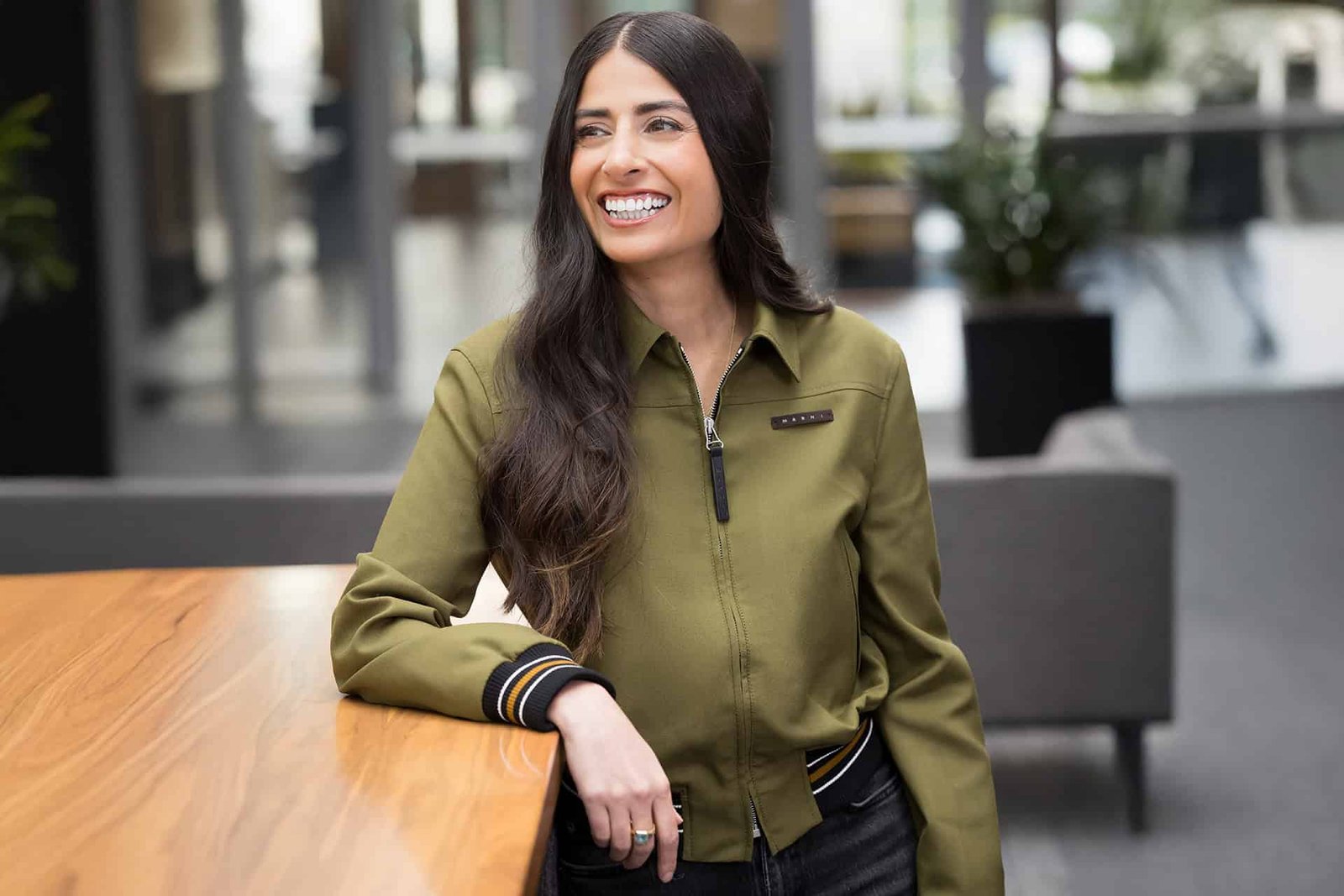 Asha Sharma smiling with one arm resting on a table